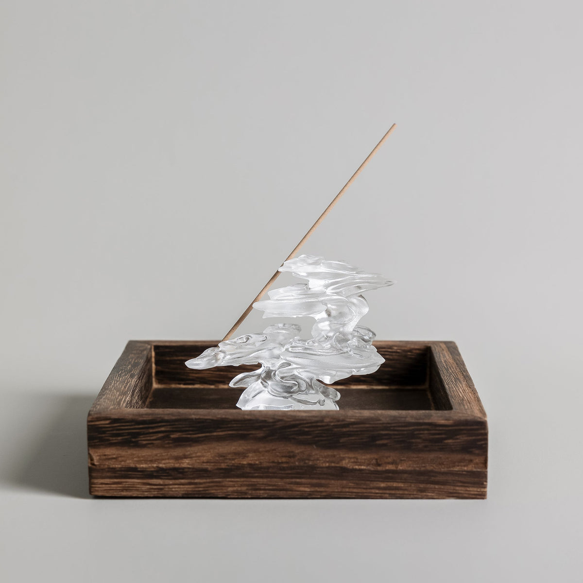 A cloud-shaped liuli glass incense burner in a wooden tray